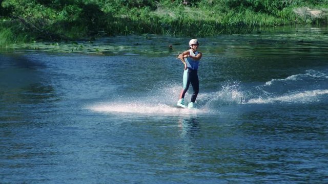 Pretty girl wakeboarding on summer river. Young girl riding water ski. Woman practicing water skiing. Slim girl wakeskier training riding on water board. Healthy lifestyle concept