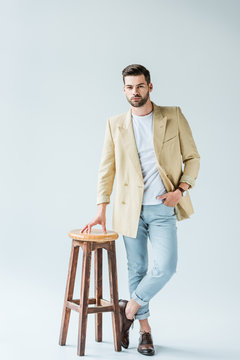 Fashionable Confident Man Leaning On Stool On White Background