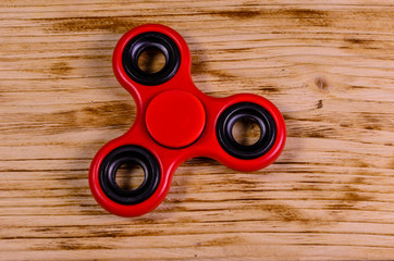 Red fidget spinner on wooden desk. Top view