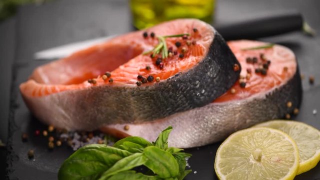Salmon. Raw trout fish steak with herbs and lemon rotated on slate. Cooking, seafood. Healthy eating concept. Rotation. Slow motion 4K UHD video 3840x2160