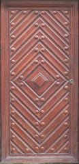 Wooden door with diamond and rivets. Red-brown color