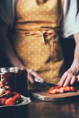 cropped image of woman in apron cutting strawberries at table