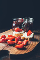 selective focus of sandwiches with cream cheese, strawberry slices and fruit jam on cutting board on black