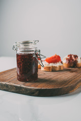 selective focus of jar with fruit jam on cutting board on grey
