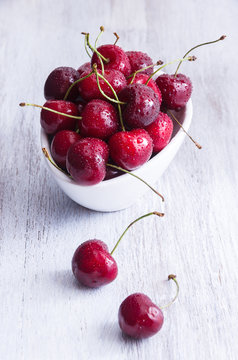 Fresh red cherry in a white bowl on wooden table