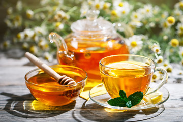 Cup with hot tea with mint and a thyme on a wooden table in a summer garden.