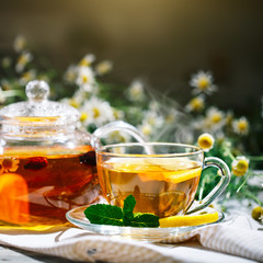Cup with hot tea with mint and a thyme on a wooden table in a summer garden.