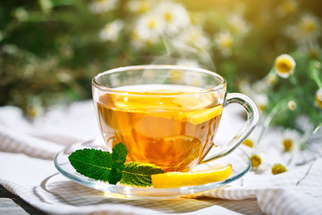 Cup with hot tea with mint and a thyme on a wooden table in a summer garden.