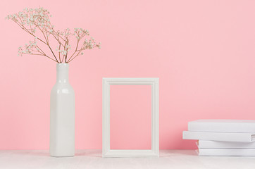 Elegance home interior of small dry flowers in vase, white books and blank wood photo frame on light pink background.