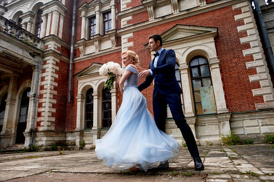 The bride and groom dancing around the columns of the old estate.A tall groom, and a bride with blond hair. Blue wedding dress.Wedding walk and photo shoot
