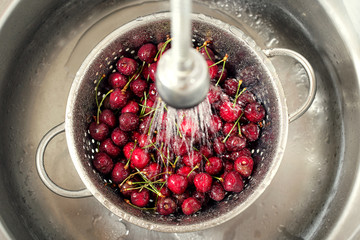 Sweet cherry washing in metal colander in the kitchen sink.