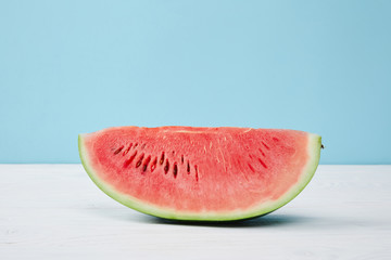 close up view of fresh watermelon slice on white surface on blue background