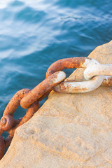 Detail of an old rusty metal chain anchored to a concrete block