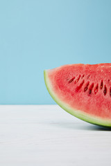 Fototapeta na wymiar close up view of fresh watermelon slice on white surface on blue background