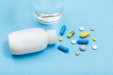 White bottle with different pills, capsules and glass of water on blue background