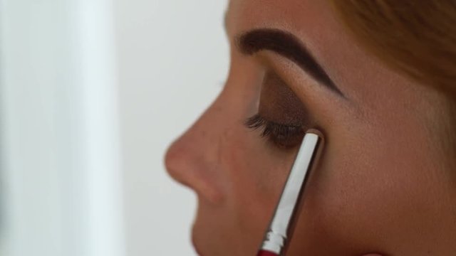 Face beautiful woman while application smoky eyes make up for beauty contest. Close up stylish makeup woman for video or photo session. Visagiste with eye shadow brush doing sexy makeup.
