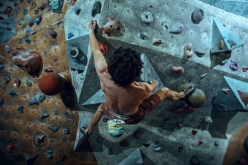 Free climber young man climbing artificial boulder indoors