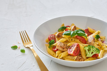 Italian food. Fusilli pasta salad with italian dressing, tomatoes, broccoli and basil leaves on white background with copy space.