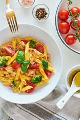Italian food. Flat lay of fusilli pasta salad with italian dressing, tomatoes, broccoli and basil leaves on white background. Top view.