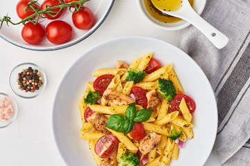 Italian food. Flat lay of fusilli pasta salad with italian dressing, tomatoes, broccoli and basil leaves on white background. Horizontal top view.