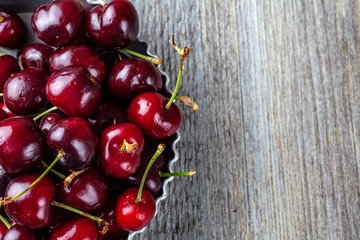 Less than perfect red cherries in a tin dish on a wooden table