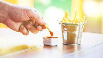 a man's hand dips potatoes into an apetitou sauce, French fries in a decorative bucket on a wooden table