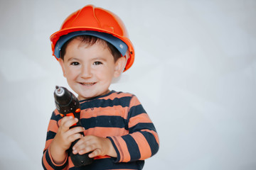 Little Boy using diy tool at home/little builder in the helmet with a drill and saw the work of thinking about the future