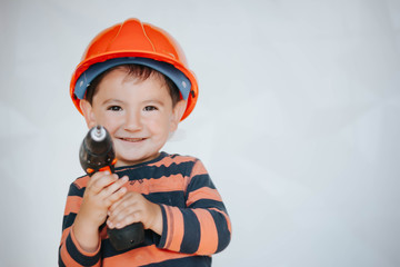 Little Boy using diy tool at home/little builder in the helmet with a drill and saw the work of...