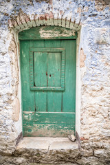 Old greenish blue wooden door and eroded wall. Front door.  Entrance to the house
