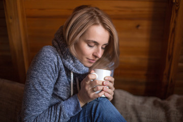 Beautiful woman with white cup sitting on couch in wooden house