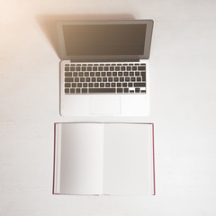 Fototapeta na wymiar Laptop with open notebook against white desk