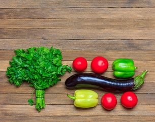 set of vegetables eggplant, tomatoes, parsley bunch and bell pepper on wooden background, top view close - up with copy space