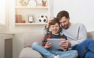 Father and son using tablet together on sofa at home