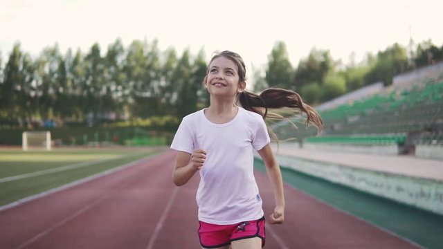 portrait of a little girl enjoys jogging. the child runs along the track at the stadium