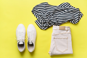 Female white sneakers and jeans, striped t-shirt on yellow background with copy space. Top view. Summer fashion, capsule wardrobe concept. Creative flat lay.