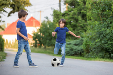 Two cute little kids, playing football together, summertime. Children playing soccer