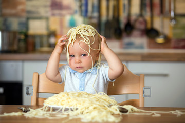 Little baby boy, toddler child, eating spaghetti for lunch and making a mess