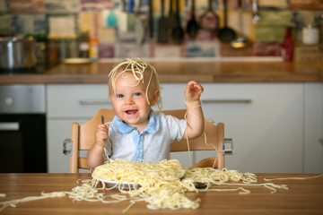 Little baby boy, toddler child, eating spaghetti for lunch and making a mess