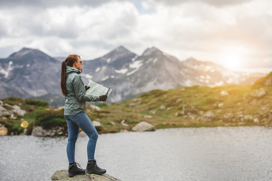 Frau steht auf Berg an einem Bergsee und orientiert sich mit Landkarte
