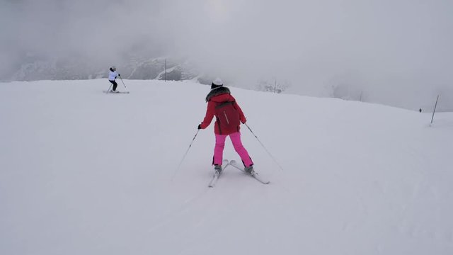 Two Sporty Female Skiers Skiing On The Mountain Downhill In Winter In Heavy Fog