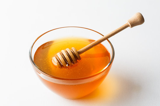Glass bowl with honey and wooden dripper spoon on white background, organic product