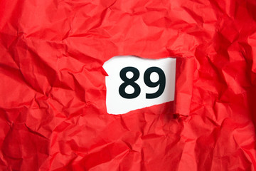 rotes zerknülltes Papier, aufgerollt mit Zahl neunundachtzig - 89 auf weißem Untergrund