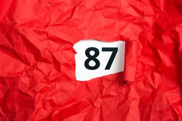 rotes zerknülltes Papier, aufgerollt mit Zahl siebenundachtzig - 87 auf weißem Untergrund