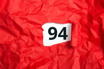 rotes zerknülltes Papier, aufgerollt mit Zahl vierundneunzig - 94 auf weißem Untergrund