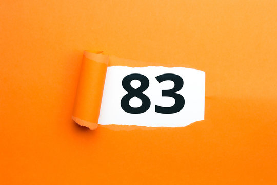Zahl dreiundachtzig - 83 verdeckt unter aufgerissenem orangen Papier