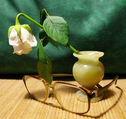 Faded rose in a vase of natural stone and glasses on straw