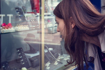 A young woman sees a store window with jewelry standing on the street.