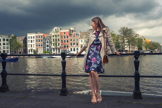 Beautiful young woman enjoying the journey, standing on the bridge in the background of the city of Amsterdam.