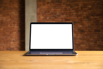 Mockup image of laptop with blank white desktop screen on wooden table with concrete wall background