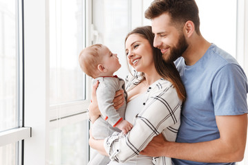 Pleased loving couple parents holding in hands their little son.